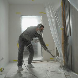 A worker in protective gear painting walls during an indoor renovation project.