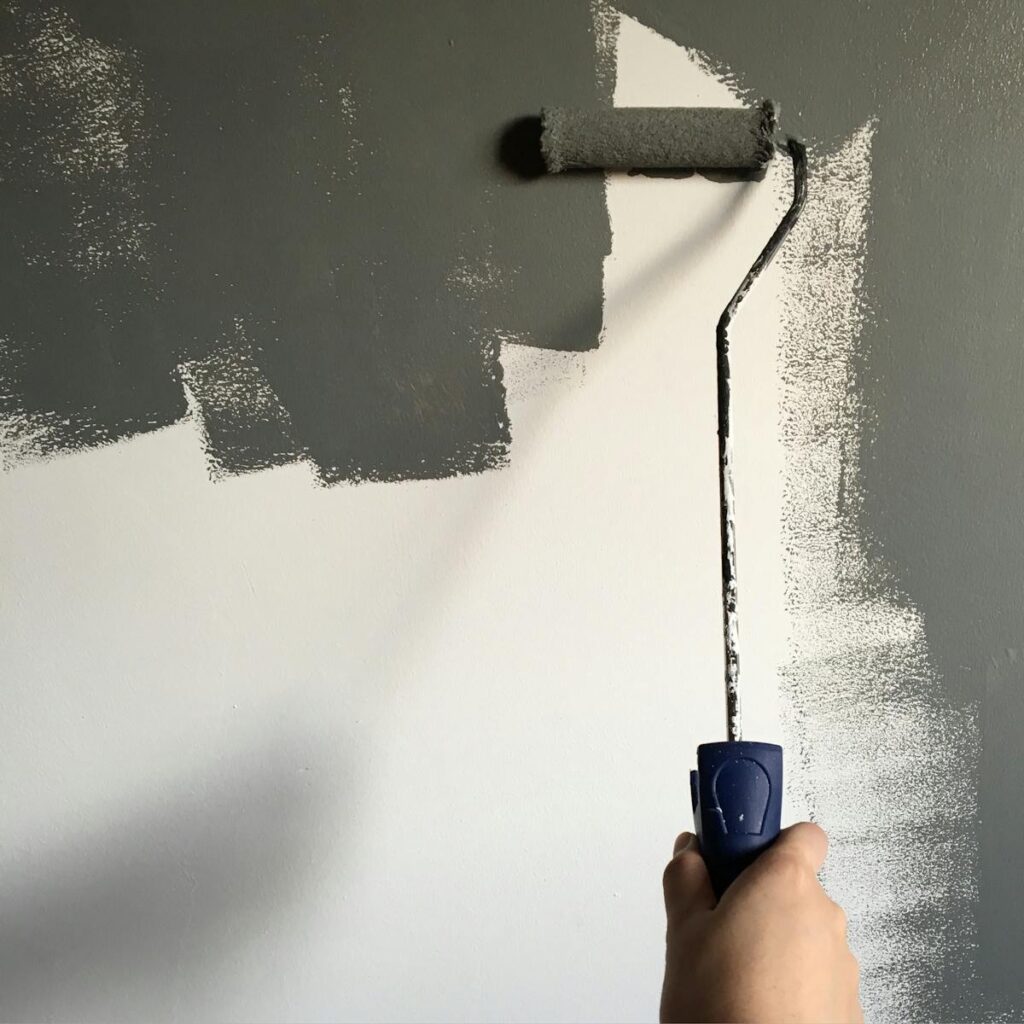 K&F reformas Foz A hand painting a wall gray with a roller during a house renovation project.